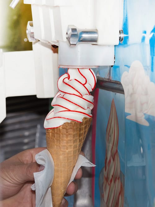 Twisted ice cream machine. Close up of hand holding cone waffle with vanilla and fruity dessert